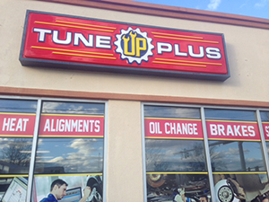 storefront window of Tune Up Plus Norfolk location with signs advertising wheel alignments, oil changes, brakes, and heating services. There are graphics of a mechanic and different parts related to these services on the window