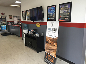 A photo from inside Tune Up Plus Norfolk. You can see the front desk and a waiting area with chairs, coffee, and a TV